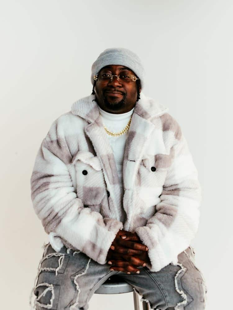 A man sitting down wearing a white coat and hat.