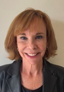 Woman with short strawberry blonde hair smiling and wearing a grey blazer.